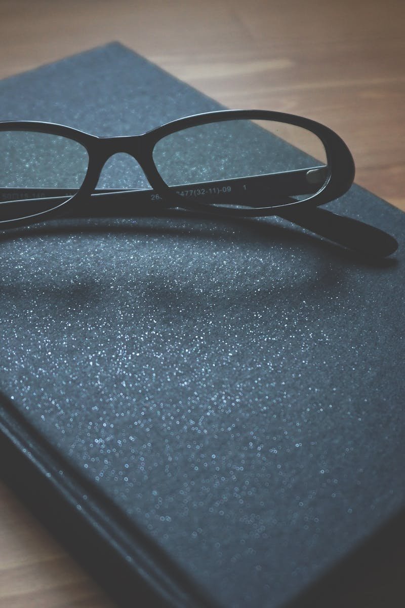 Black notebook with eyeglasses on a wooden surface, capturing a professional and classic vibe.